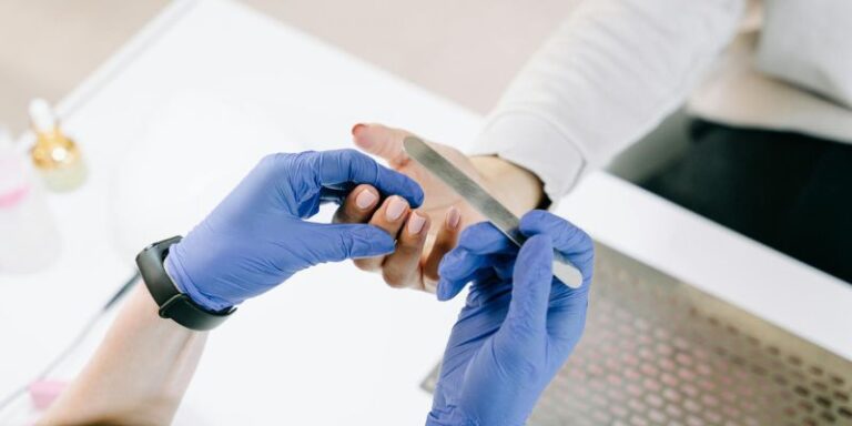 Nail Care - A Person in Blue Gloves Holding a Nail File And Using it to Her Client