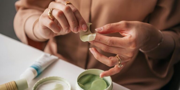 Close-up of Woman Holding an Under Eye Patch and Sitting at a Table with Cosmetics