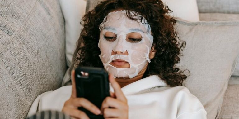 Beauty Tech - Woman in hydrating sheet mask browsing smartphone