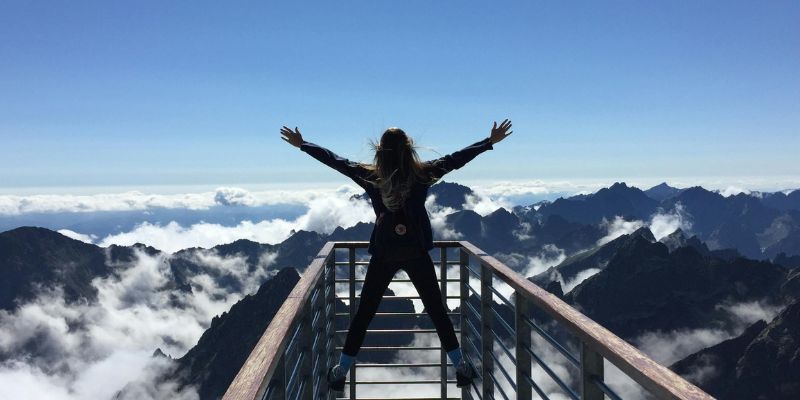 Best Version of Yourself - Person Standing on Hand Rails With Arms Wide Open Facing the Mountains and Clouds