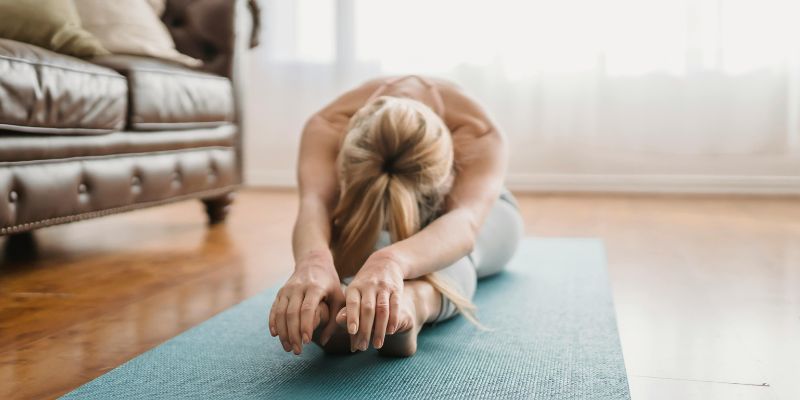 Types of stretches - Flexible lady practicing Pascimottanasana yoga pose at home