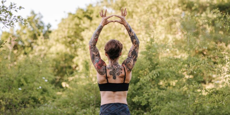Yin yoga - Unrecognizable tattooed woman practicing yoga against lush trees