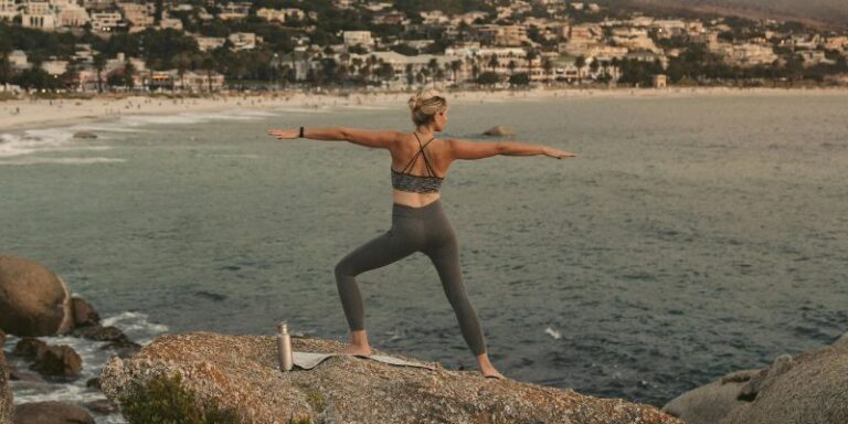 Yoga Travel - A Woman Doing a Warrior Pose on a Rock